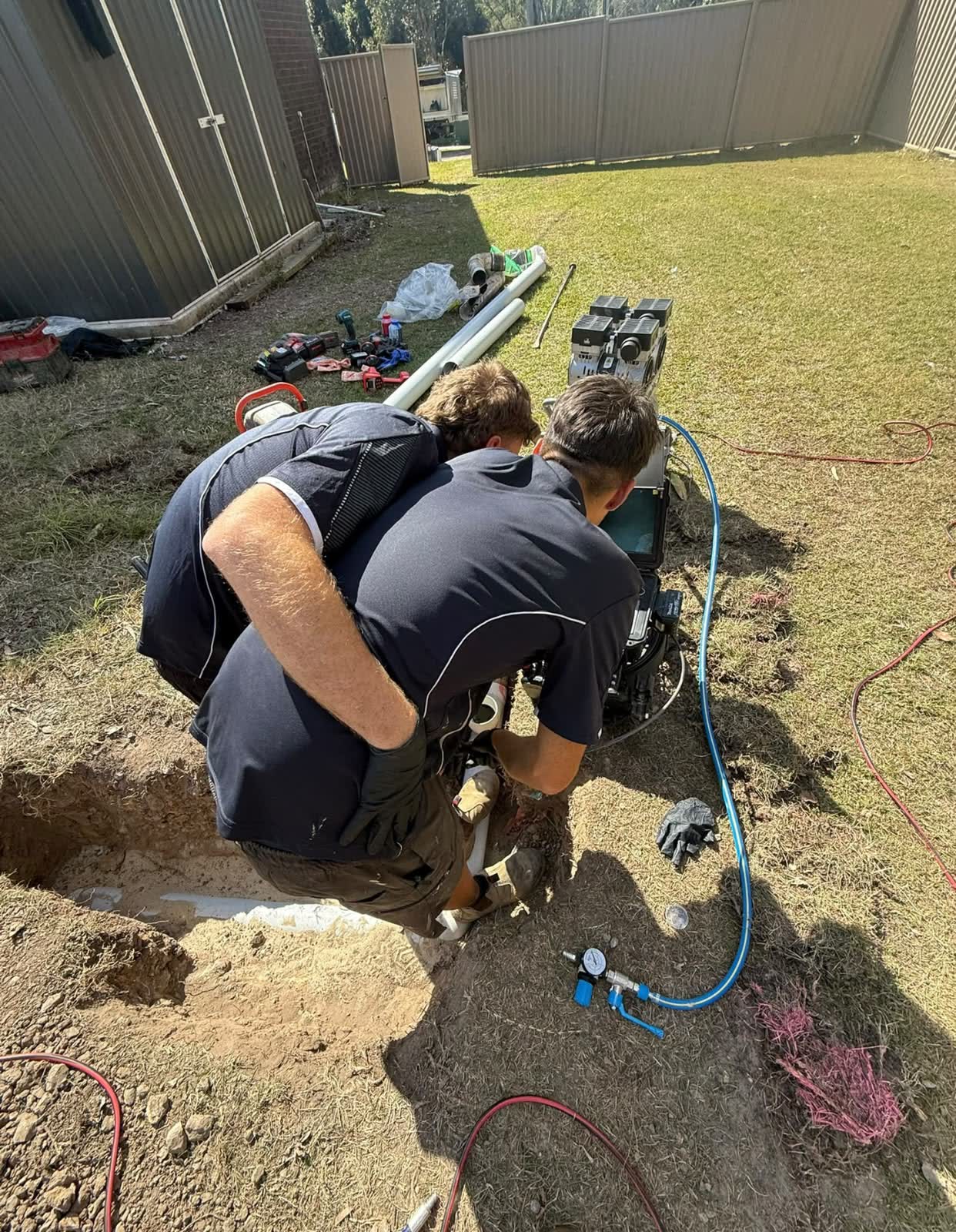 Two plumbers repairing a drain in a dug-out trench